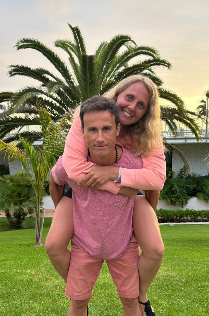 Sébastien Mot portant sa femme sur son dos, devant un palmier au coucher du soleil